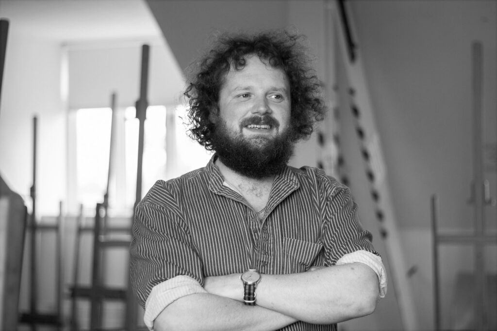 Black and white photo of the poet Scott McKendry smiling with his arms crossed across his chest